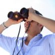man on beach looking through binoculars with sun spots_canstockphoto525383 275x270